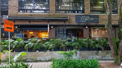 a restaurant with palm trees in front of a building at Económicas habitaciones amobladas en Medellín con oficinas, puesto de trabajo, cocina, baño y lavandería comunes Be Together by Roots Rentals TOG401y402 in Medellín