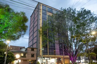 a tall glass building with trees in front of it at Comfortable Escape | Rosa Negra Stadio ApartaSuite in Medellín
