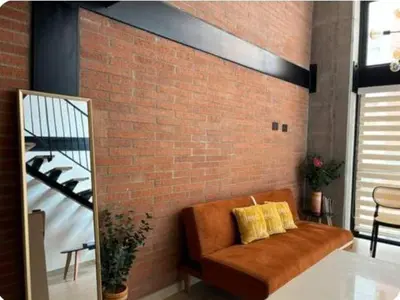 a brown couch with two yellow pillows on a brick wall at Loft hermoso y céntrico 1109 in Medellín