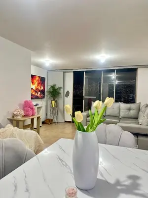 a white vase with flowers on a table in a living room at Apartamento cerca del estadio de Medellín in Medellín