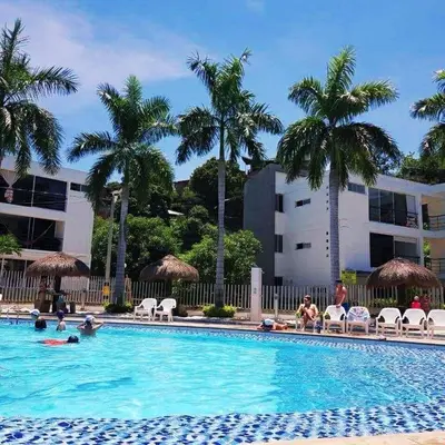 a swimming pool with palm trees and people sitting in chairs at Apartasol Santafe de Antioquia in Santa Fe de Antioquia