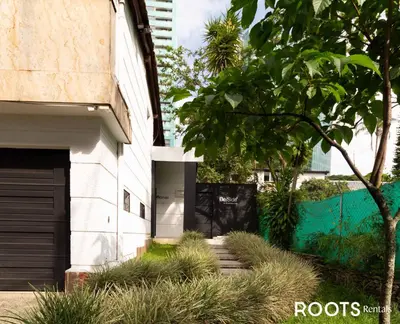 a white building with a garage and a tree at Económico alojamiento en Medellín por días - A102 By Roots Rentals in Medellín